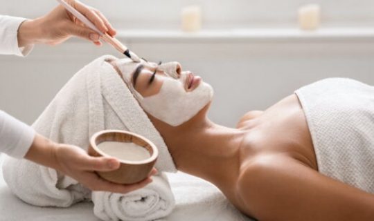 Facial treatment. Beautician applying clay face mask to asian woman at spa